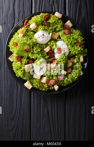 Insalata Gourmet Lyonnaise con lattuga, bacon croccante, crostini e uova in camicia di close-up su una piastra sul tavolo. Verticale in alto vista da sopra Foto Stock
