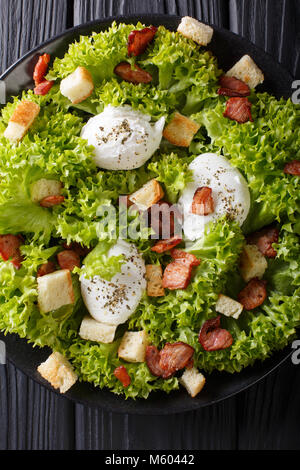 Insalata francese Lyonnaise con lattuga, bacon croccante, crostini e uova in camicia di close-up su una piastra sul tavolo. Verticale in alto vista da sopra Foto Stock