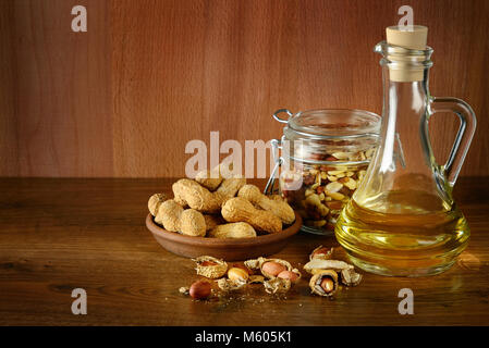 Olio di arachidi in bottiglia e frutta secca su un tavolo di legno. Spazio di copia Foto Stock