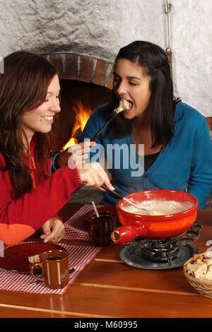 Foto di due bellissime femmine intingere il pane nel formaggio fuso in una fondue pot. Focus è la ragazza sulla destra. Foto Stock