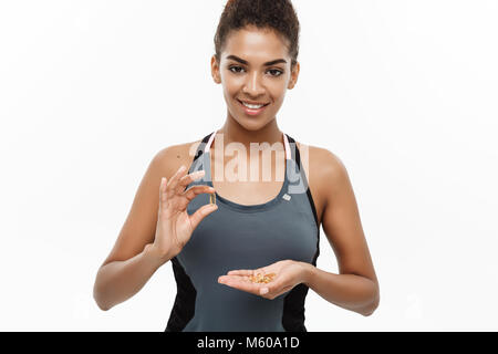 Sana e concetto di Fitness - Closeup ritratto della bella americano africano di prendere una pillola di olio di fegato di merluzzo. Isolato su bianco di sfondo per studio. Foto Stock