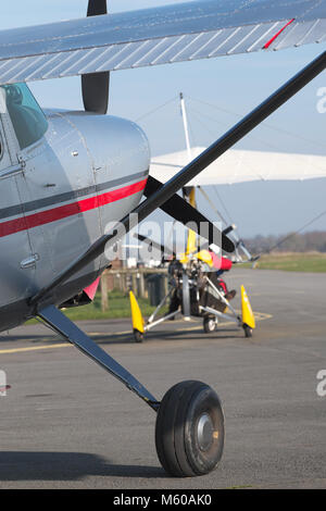 Aviazione generale Cessna 185 aeromobili leggeri con un giallo ala flessibile ultraleggero dietro su airfield grembiule Foto Stock