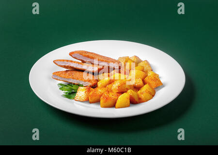 Cotoletta con patate fritte su una piastra bianca su sfondo verde. Vista laterale. Guarnito con vegetazione. Foto Stock