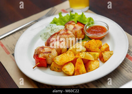 Barbecue di carne di maiale, carne di manzo con patate fritte su una piastra bianca. Un pasto abbondante cena. Il piatto per il menu. Vista laterale. Close up Foto Stock