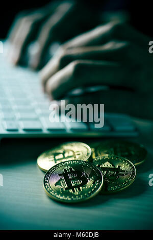 Primo piano di una pila di bitcoins e un giovane uomo che utilizza un computer in background, con un effetto drammatico Foto Stock