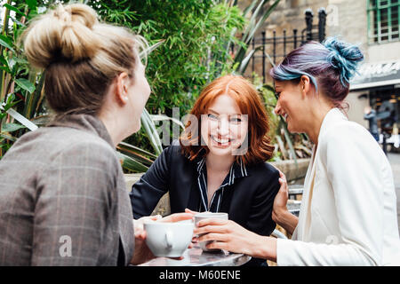 Tre donne di business stanno godendo una pausa caffè insieme nella città. Essi sono qui seduti nell'area esterna e di un cafe e sono tutti a ridere e parlare Foto Stock