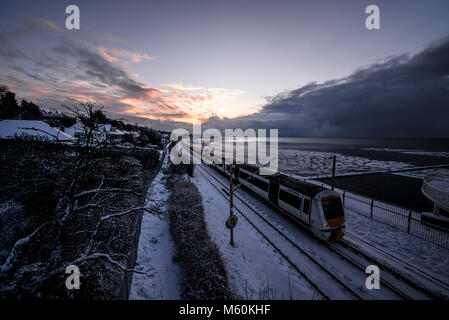 Treno nella neve. C2C convoglio ferroviario in esecuzione attraverso la coperta di neve linee in Chalkwell vicino a Southend on Sea, Essex all'alba accanto all'estuario del Tamigi Foto Stock