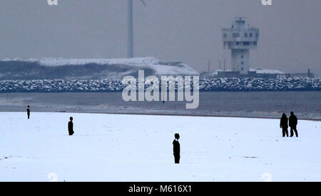 Walkers nella neve vicino a un altro luogo da Anthony Gormley, su Crosby il faggio vicino al Liverpool, a seguito di una notte pesante nevicata che ha provocato interruzioni in tutta la Gran Bretagna. Foto Stock