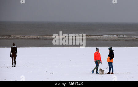 Dog walkers nella neve accanto a un altro luogo da Anthony Gormley, su Crosby il faggio vicino al Liverpool, a seguito di una notte pesante nevicata che ha provocato interruzioni in tutta la Gran Bretagna. Foto Stock