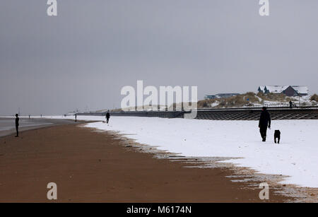 Dog walkers nella neve vicino a un altro luogo da Anthony Gormley, su Crosby il faggio vicino al Liverpool, a seguito di una notte pesante nevicata che ha provocato interruzioni in tutta la Gran Bretagna. Foto Stock