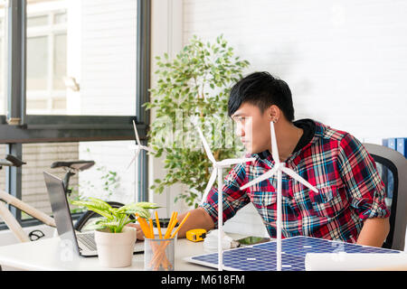 Maschio asiatici green power engineer a utilizzare il computer per la progettazione di un nuovo mulino a vento in studio office Foto Stock