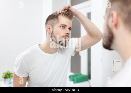 Bello barba lunga uomo guardando nello specchio nella stanza da bagno Foto Stock