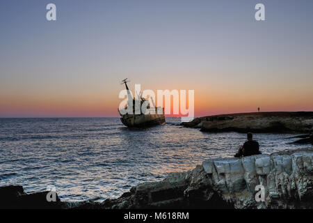 Uomo seduto a guardare il tramonto sul punto di riferimento naufragio a Pafos, Cipro. Foto Stock