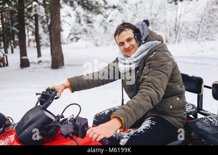 La faccina sorridente nella neve e nel ghiaccio dopo in sella a una coperta di neve foresta su una motocicletta in inverno Foto Stock