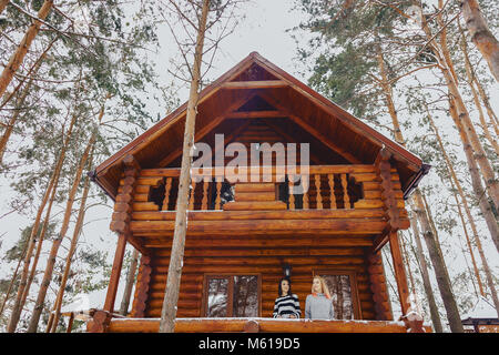 Le ragazze è venuto fuori un cottage di legno casa sullo sfondo della coperta di neve alberi di pino Foto Stock