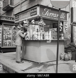 Degli anni Cinquanta, storico, Napoli, Italia, un uomo di bere presso un chiosco di strada di Ferrarelle, un Italiano scintillante acqua minerale. L'acqua dalla Val d'Assano, Napoli ha un sapore unqiue provenienti come fa da rocce vulcaniche e naturalmente gasata con 100% delle sue bolle creata dalla natura. Foto Stock