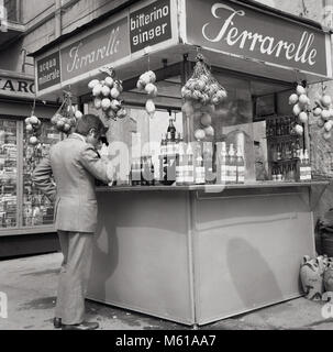 Degli anni Cinquanta, storico, Napoli, Italia, un uomo di bere presso un chiosco di strada di Ferrarelle, un Italiano scintillante acqua minerale. L'acqua dalla Val d'Assano, Napoli ha un sapore unqiue provenienti come fa da rocce vulcaniche e naturalmente gasata con 100% delle sue bolle creata dalla natura. Foto Stock