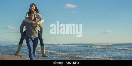 Gli uomini dando Piggy Back corse al tramonto sul mare, tempo di autunno Foto Stock