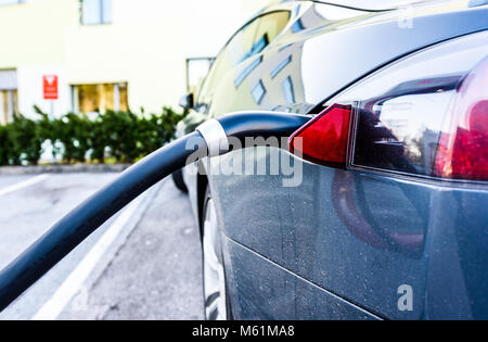 Ricarica auto elettrica con ricarica nero del cavo elettrico collegato alla presa di corrente. Ricarica costoso moderno veicolo elettrico in un parcheggio. Foto Stock