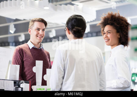 Felice il cliente a parlare con due utili ai farmacisti in farmacia contemporaneo Foto Stock