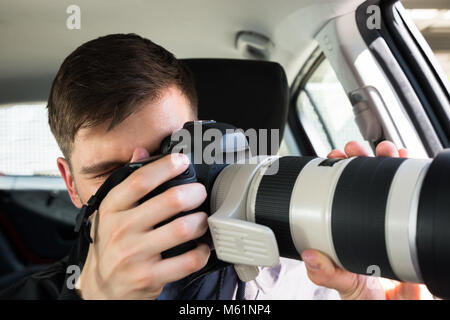 Vista laterale di un detective privato seduto all'interno dell'auto fotografare con SLR Fotocamera Foto Stock