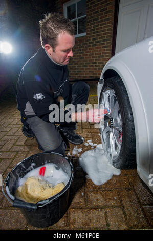 Auto valeter utilizzando una barra di argilla sulla ruota mentre che dettaglia una Porsche auto sportiva Foto Stock