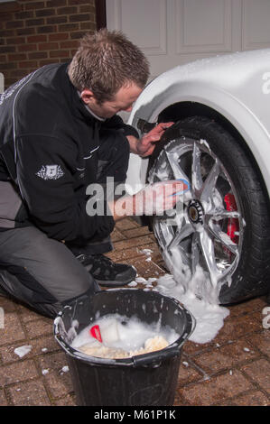 Auto valeter utilizzando una barra di argilla sulla ruota mentre che dettaglia una Porsche auto sportiva Foto Stock