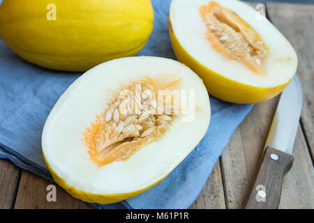 Mature organico melone freschi interi e tagliati a metà sul tovagliolo blu coltello sulla tavola di legno Tavolo da giardino. Estate Frutta di stagione Harvest vitamine dieta sana C Foto Stock