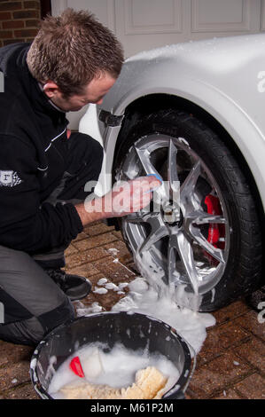 Auto valeter utilizzando una barra di argilla sulla ruota mentre che dettaglia una Porsche auto sportiva Foto Stock