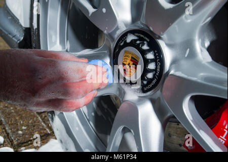 Auto valeter utilizzando una barra di argilla sulla ruota mentre che dettaglia una Porsche auto sportiva Foto Stock