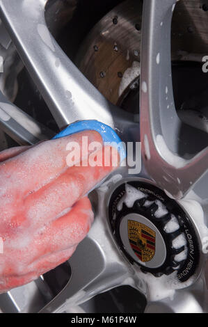 Auto valeter utilizzando una barra di argilla sulla ruota mentre che dettaglia una Porsche auto sportiva Foto Stock