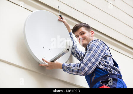 Giovane Maschio tecnico in uniforme di installazione TV Satellitare sulla parete Foto Stock