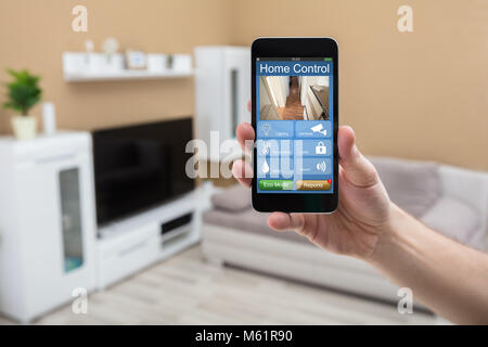 Close-up di una mano umana tenendo il telefono cellulare con la Home del sistema di controllo sullo schermo Foto Stock