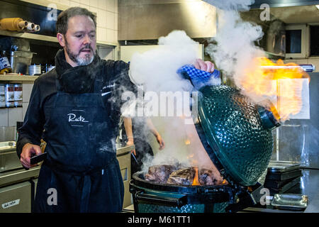 Il tedesco 3 Michelin Star chef Marco Müller nel suo elemento: Big Green Egg sotto il fuoco. Uno dei segreti del brisket di manzo tenero è l'ordine 'inverso': Prima riscaldarlo nel forno a fuoco basso e poi grigliarlo caldo nel proprio fumo appena prima di tagliarlo Foto Stock