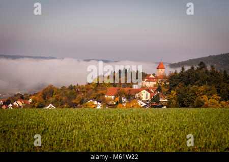 Burg Wernberg castello tedesco in Baviera in un wafer di nebbia. Il verde paesaggio collinare del Palatinato superiore e del Castello di Wernberg nel mezzo della nebbia mattutina Foto Stock