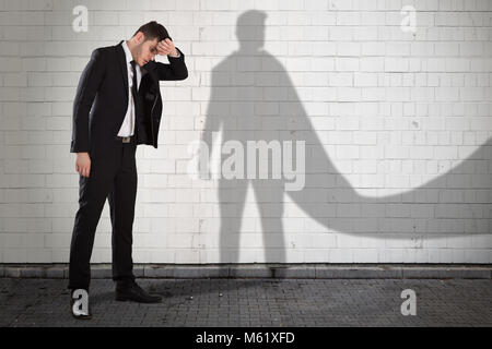 Giovani stanchi imprenditore con la sua ombra in Superhero Cape Foto Stock