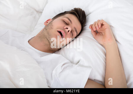 Vista stanco giovane uomo russare mentre profonde dormire nel letto Foto Stock