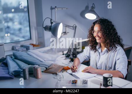 Ridendo donna scrivere appunti a personalizzare il tavolo la sera Foto Stock