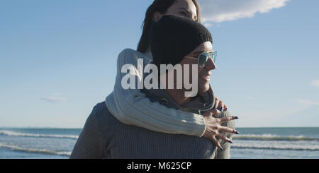 Gli uomini dando Piggy Back corse al tramonto sul mare, tempo di autunno Foto Stock