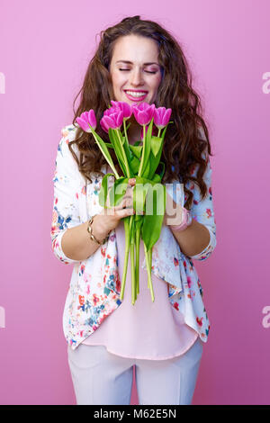 Rosa umore. sorridente giovane donna con lunghi mossi brunette capelli su sfondo rosa godendo di un bouquet di tulipani Foto Stock