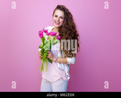 Rosa dell'umore. Ritratto di sorridere alla moda di donna con lunghi mossi brunette capelli su sfondo rosa con un bouquet di tulipani Foto Stock