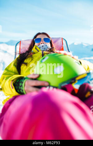 Ritratto di sport con i capelli lunghi brunette con casco in appoggio su una sedia in inverno resort Foto Stock