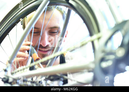 Il meccanico in un negozio di riparazione di biciclette oliatura della catena di una bicicletta Foto Stock