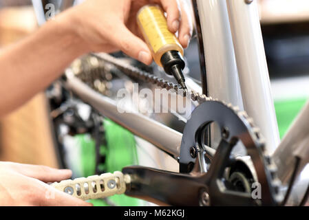 Il meccanico in un negozio di riparazione di biciclette oliatura della catena di una bicicletta Foto Stock