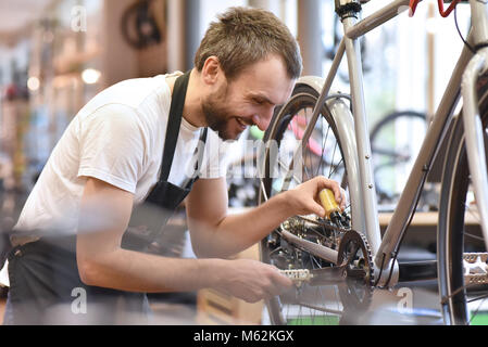 Il meccanico in un negozio di riparazione di biciclette oliatura della catena di una bicicletta Foto Stock