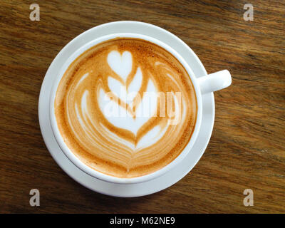 Un delizioso caffè cappuccino con latte bianco decorazione foglia sulla tazza bianca e la piastra su sfondo di legno Foto Stock
