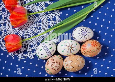 Colorate le uova di Pasqua con i tulipani sulla tovaglia blu. Foto Stock