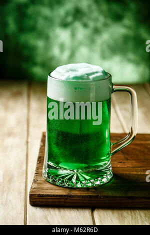 Primo piano di un vasetto di vetro con tinta verde birra su di un rustico in legno superficie contro uno sfondo verde con un po' di spazio vuoto sulla parte superiore Foto Stock