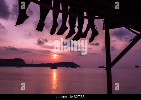 Gruppo di amici seduti sul dock di baia godendo incantevole tramonto nell'isola di Koh Samui, Thailandia. Tranquillo e calmo vacanze estive concept Foto Stock