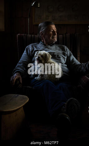 Il vecchio uomo si appoggia a casa posti a sedere sulla poltrona in salotto con il bianco piccolo cane Maltese per il suo giro. Il concetto di comfort. Bassa immagine chiave Foto Stock